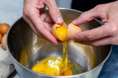 Cracking fresh eggs into a mixing bowl to prepare traditional French crepe batter.