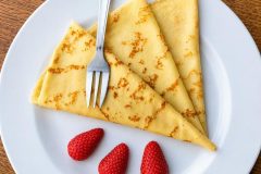 Homemade Breton crepes folded and served on a plate with fresh strawberries.