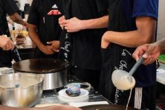 Participants apprenant à étaler une crêpe sur une billig pendant un atelier de crêpes à Paris.