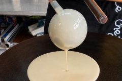Versement de la pâte sur une billig au début de la cuisson d'une crêpe bretonne.